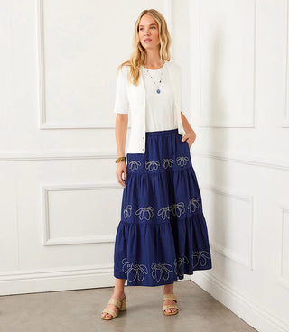 A woman wearing an off-white short sleeve ribbed cardigan sweater with a V-neck, paired with a blue skirt with decorative white detail.