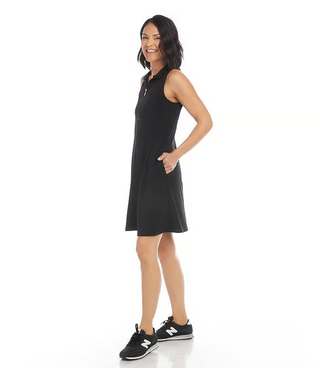 A woman standing and wearing a sleeveless black dress with a zip-up neckline, and black shoes.