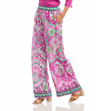 A pair of high-waisted, wide-leg pants with a paisley print in pink and green hues on a crepe fabric. They feature a pull-on elastic waistband