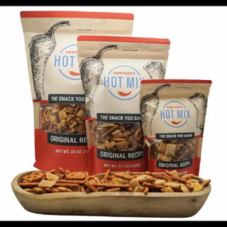 Three packages of Kentucky Hot Mix snack mix with a wooden bowl of snacks in front. Kentucky Hot Mix Assorted