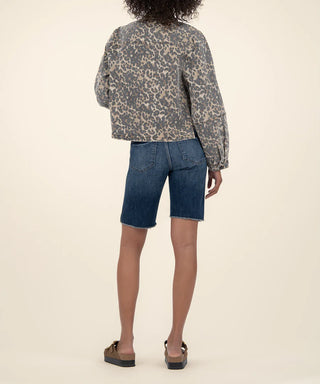 Person wearing a Kut tan and brown animal patterned jacket and blue denim shorts on a beige background, view of back