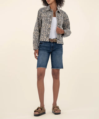 Person wearing a Kut tan and brown animal patterned jacket, white top, blue denim shorts, and brown sandals on a beige background