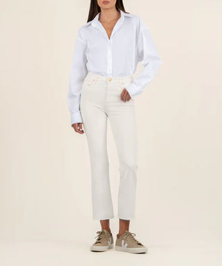 A female model wearing a white shirt and ecru high-rise ankle flare jeans with a raw hem.