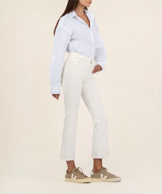 A female model wearing a white shirt and ecru high-rise ankle flare jeans with a raw hem.