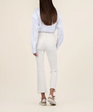 A female model wearing a white shirt and ecru high-rise ankle flare jeans with a raw hem.