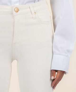A female model wearing a white shirt and ecru high-rise ankle flare jeans with a raw hem.