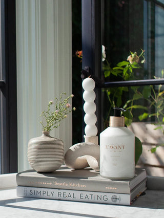 White bottle labeled 'LAVANT' on books with decorative items in a home setting