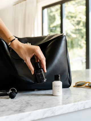 Person holding a black bottle labeled 'L'AVANT' next to a white bottle on a marble surface.
