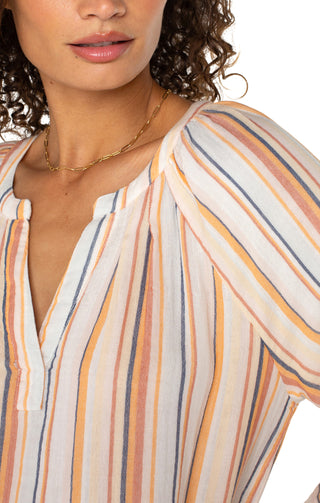 A woman wearing a multicolor striped Liverpool woven top with 3/4 sleeves and a V-neckline, paired with white shorts.