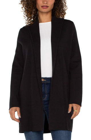 A woman wearing a Liverpool black long sleeve open front shawl sweater coatigan over a white top, paired with blue jeans.