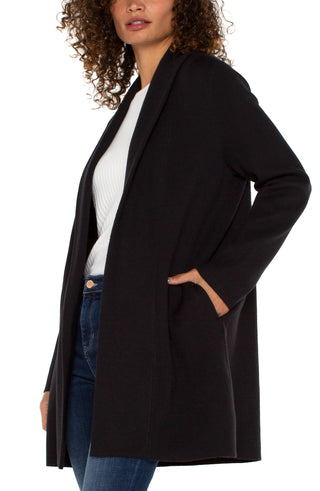 A woman wearing a Liverpool black long sleeve open front shawl sweater coatigan over a white top, paired with blue jeans.