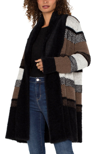 A woman wearing a long sleeve open front shawl sweater coatigan with a fuzzy jacquard pattern in black and tan colors, paired with blue jeans.