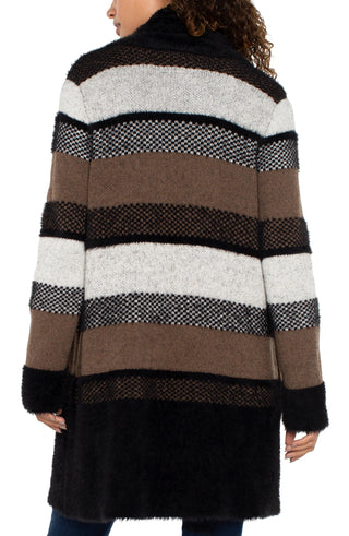 A woman wearing a long sleeve open front shawl sweater coatigan with a fuzzy jacquard pattern in black and tan colors, paired with blue jeans.
