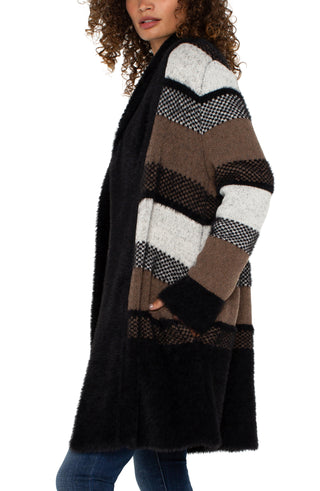 A woman wearing a long sleeve open front shawl sweater coatigan with a fuzzy jacquard pattern in black and tan colors, paired with blue jeans.