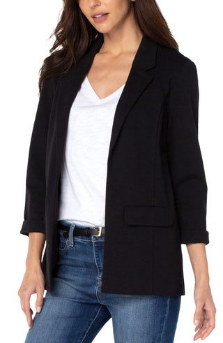 A woman wearing a black boyfriend blazer with princess darts, paired with a white top and blue jeans.