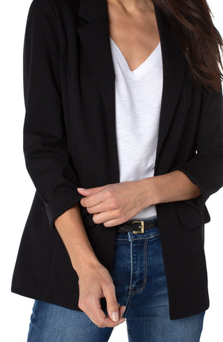 A woman wearing a black boyfriend blazer with princess darts, paired with a white top and blue jeans.