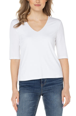 A woman wearing a white v-neck knit top with half sleeves and elbow sleeves, paired with blue jeans.