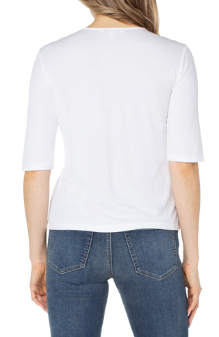 A woman wearing a white v-neck knit top with half sleeves and elbow sleeves, paired with blue jeans.