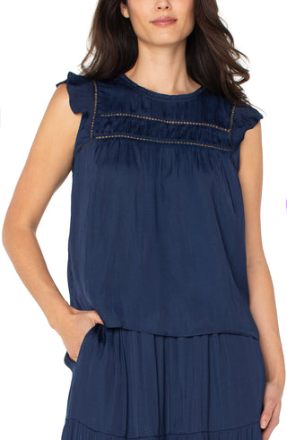 Woman wearing a navy blue top with ruffled shoulders on a white background