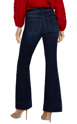 A pair of dark wash flare jeans with pintucks, featuring a mid-rise waist, 5-pocket styling, and a zip fly with a single button closure. The jeans are modeled with a heel.
