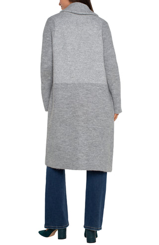 A woman wearing a long sleeve grey pattern open front shawl sweater coatigan with a white top and blue jeans.