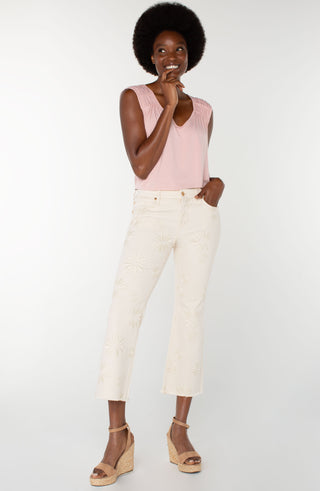 A pair of ecru colored crop flare jeans with floral embroidery and a frayed hem, featuring a mid-rise waist and a pair of tan sandals.