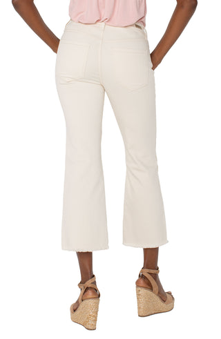 A pair of ecru colored crop flare jeans with floral embroidery and a frayed hem, featuring a mid-rise waist and a pair of tan sandals.