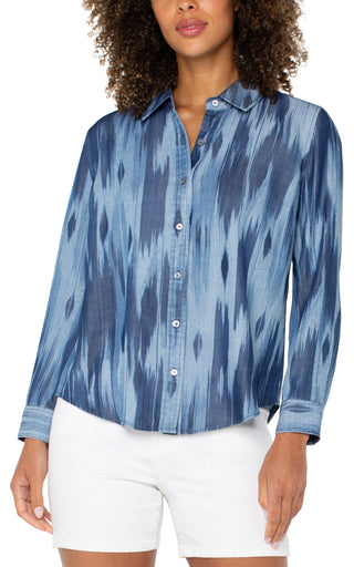 A woman's long rolled sleeve woven shirt with a water color ikat print in blue tones.