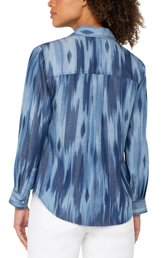 A woman's long rolled sleeve woven shirt with a water color ikat print in blue tones.
