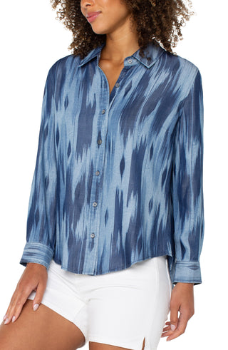 A woman's long rolled sleeve woven shirt with a water color ikat print in blue tones.