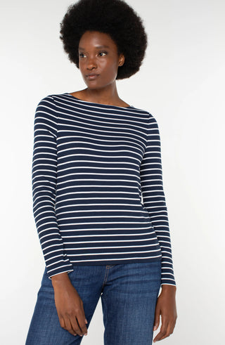 A woman wearing a dark navy long sleeve boatneck knit top with white stripes, paired with jeans.