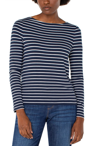 A woman wearing a dark navy long sleeve boatneck knit top with white stripes, paired with jeans.