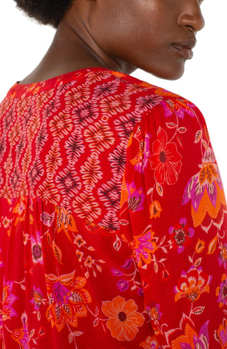 A woman wearing a red orange floral long sleeve button front shirred blouse with a V-neck.