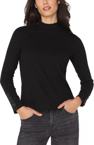 Woman wearing a black ribbed sweater and dark jeans on a white background