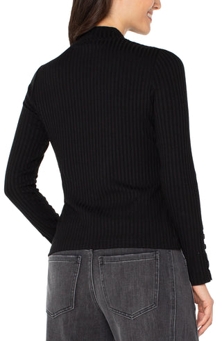 Person wearing a black ribbed sweater and gray jeans on a white background