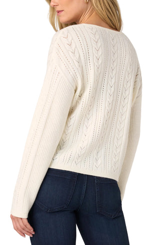 Liverpool Long Sleeve V-neck Drop Shoulder Sweater in Cream
A woman wearing a cream cable-knit sweater and dark blue jeans, shown from a back three-quarter angle against a light gray studio background.