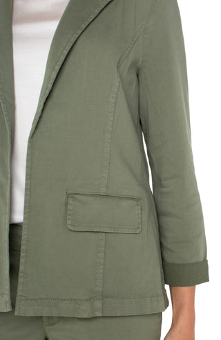 A model in a fitted olive green blazer with rolled sleeves and front pockets.