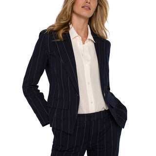 A woman wearing a navy striped blazer with a notch collar and one button closure, paired with a white shirt.