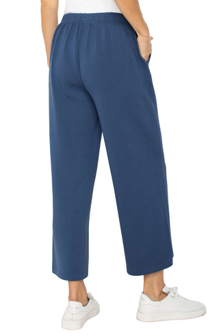 A person standing and wearing the Liverpool Pull On Wide Leg Crop Trouser in Prussian Blue with white sneakers.