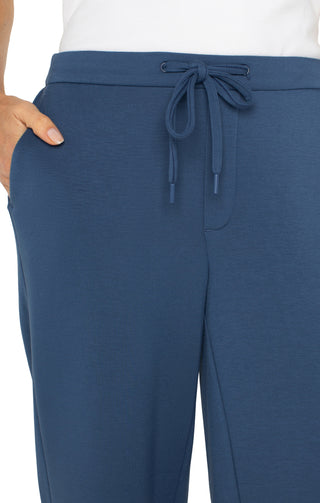 A person standing and wearing the Liverpool Pull On Wide Leg Crop Trouser in Prussian Blue with white sneakers.