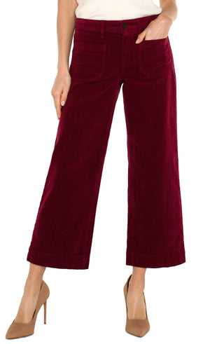 A pair of ruby red corduroy crop wide-leg pants with patch pockets, featuring a mid-rise waist and a flared leg design.
