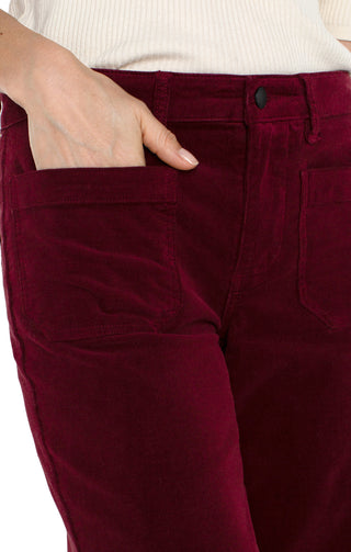 A pair of ruby red corduroy crop wide-leg pants with patch pockets, featuring a mid-rise waist and a flared leg design.