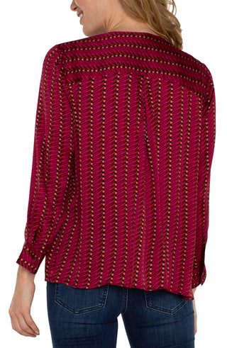 A woman wearing a red long sleeve blouse with a stripe and dot pattern, featuring a jewel neck and popover design.