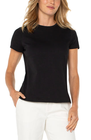 A woman wearing a short sleeve black crew neck t-shirt paired with white pants.