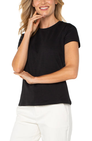 A woman wearing a short sleeve black crew neck t-shirt paired with white pants.