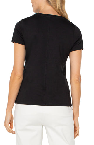 A woman wearing a short sleeve black crew neck t-shirt paired with white pants.