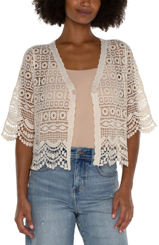 A woman wearing an antique ivory short sleeve lace bolero over a white top, paired with blue jeans.