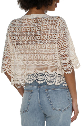 A woman wearing an antique ivory short sleeve lace bolero over a white top, paired with blue jeans.