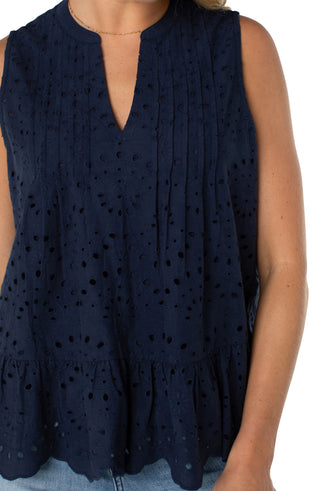 A navy, sleeveless woven top with pintuck details and a scalloped edge finish, worn by a model paired with jeans.