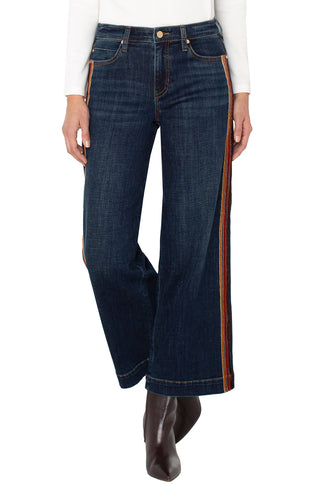 Dark blue jeans with brown side stripes worn by a person on a white background